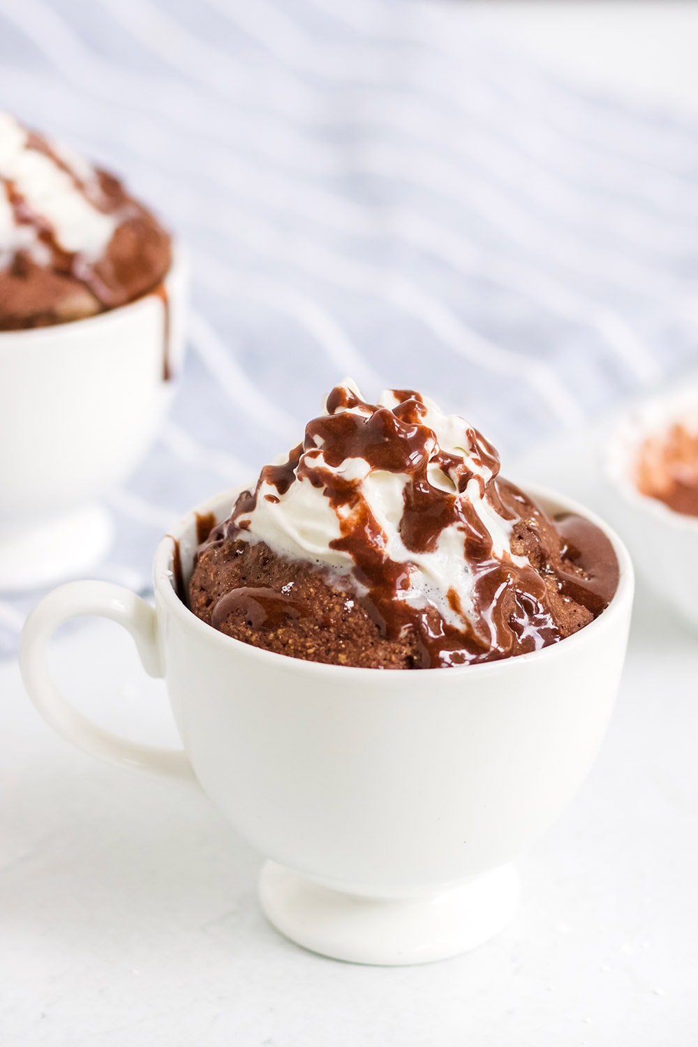 Low-carb chocolate mug cake with glaze and whipped topping.