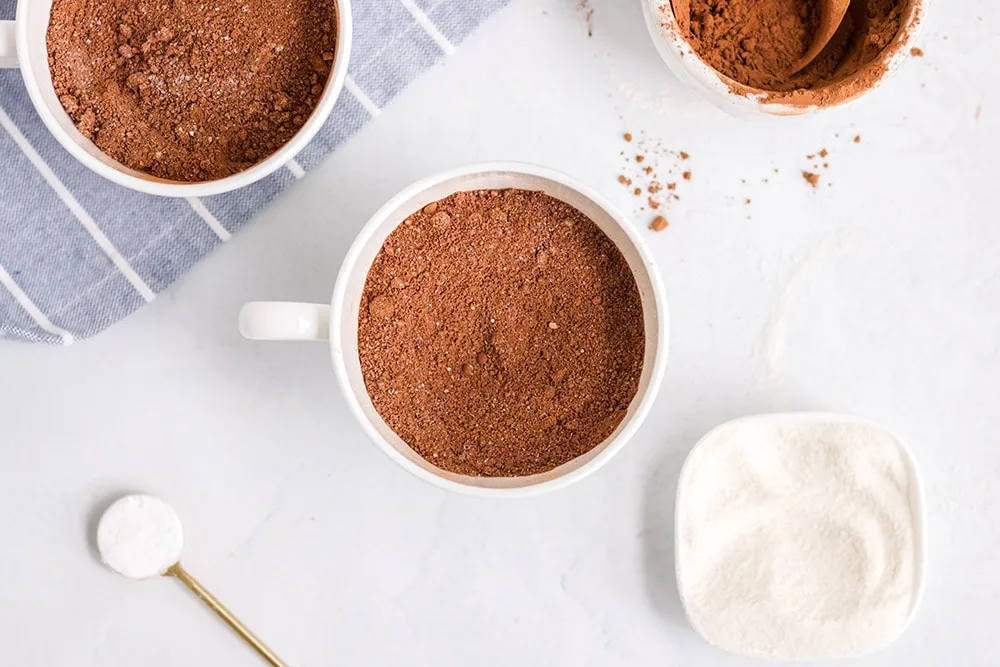 Cocoa powder in a mug next to other mug cake ingredients.