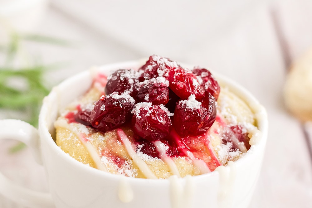 Cake topped with cranberries in a white mug. 