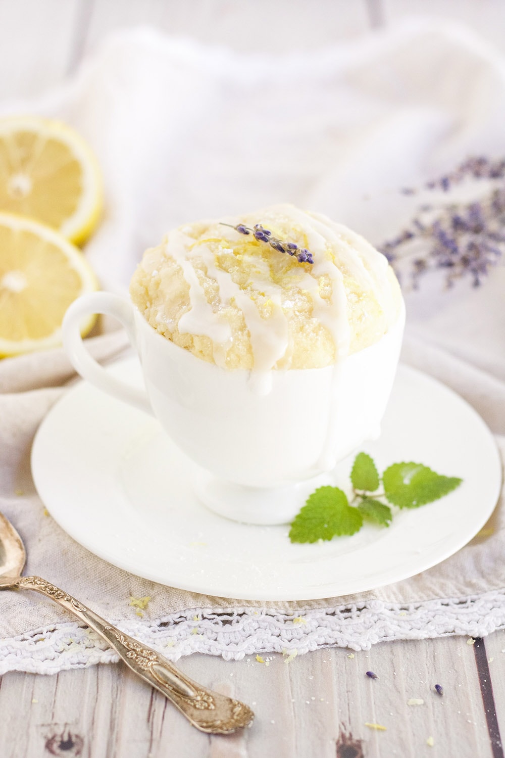 Lemon cake in a mug with lemons and lavender around on the table.