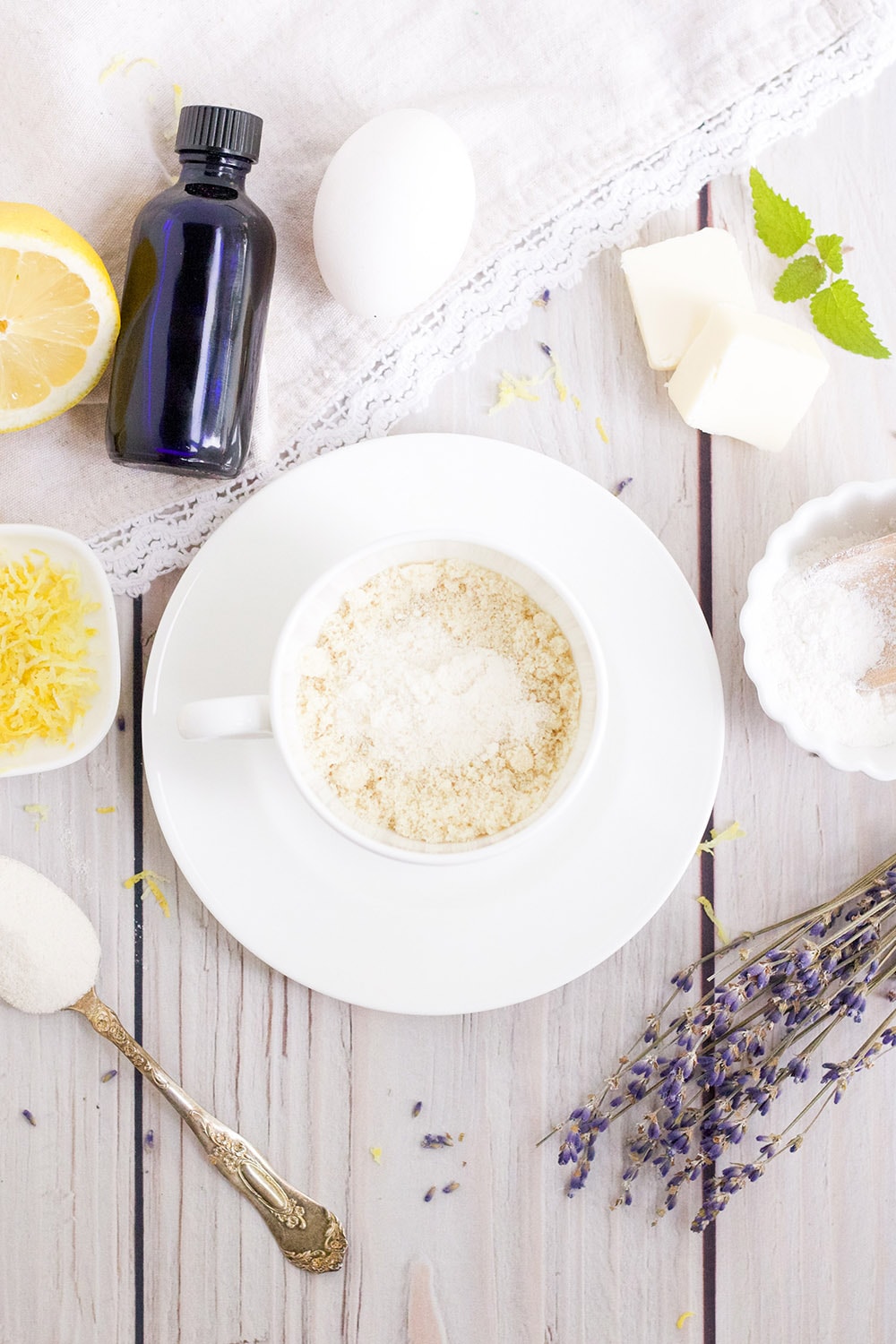 Dry ingredients in mug with dried lavender, lemon, and other ingredients on table.
