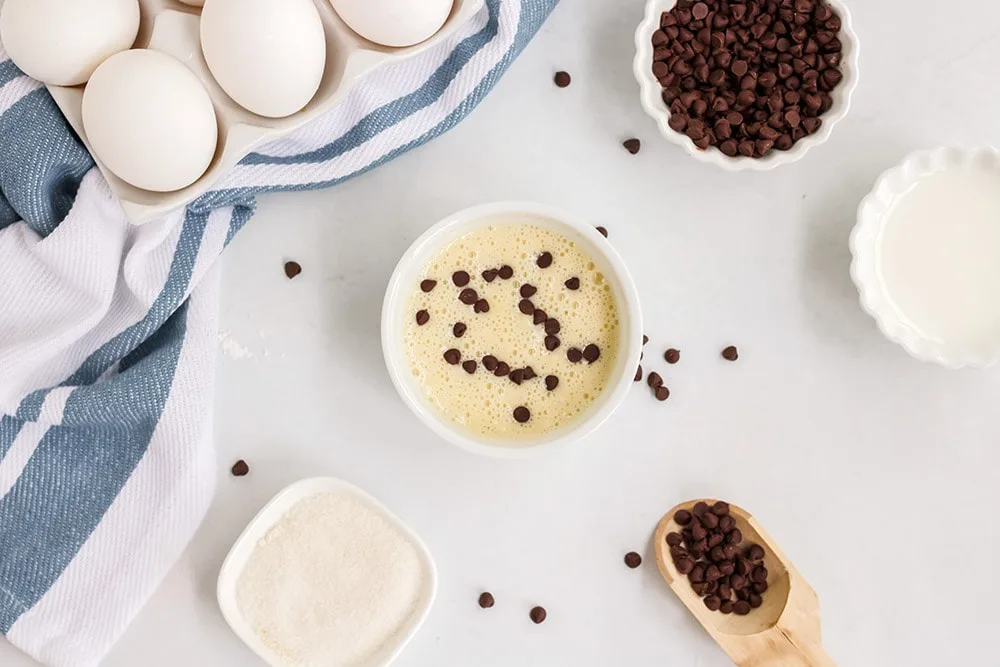 Mug cake batter in a ramekin with chocolate chips and other ingredients on a table.