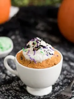 pumpkin cake in a mug topped with Halloween colored coconut shreds