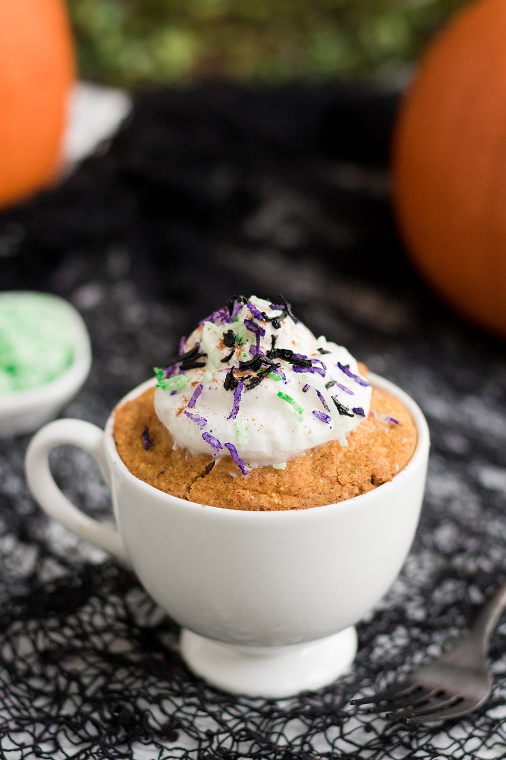 Pumpkin cake in a mug topped with Halloween colored coconut shreds.