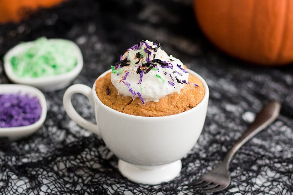 pumpkin cake in a mug topped with whipped cream and halloween colored shavings