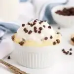 Keto chocolate chip mug cake with chocolate chips on top of whipped cream next to milk and more chips