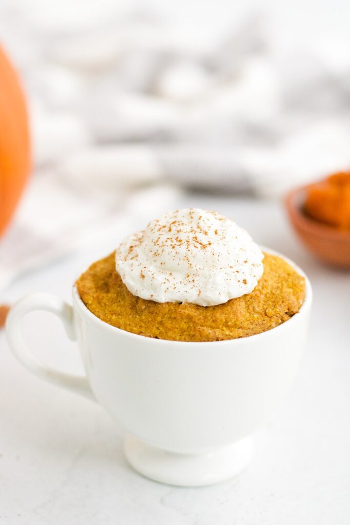keto pumpkin mug cake in a white mug topped with whipped cream