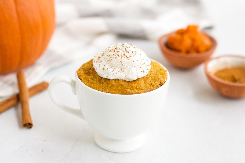 Pumpkin cake in a mug topped with whipped cream.