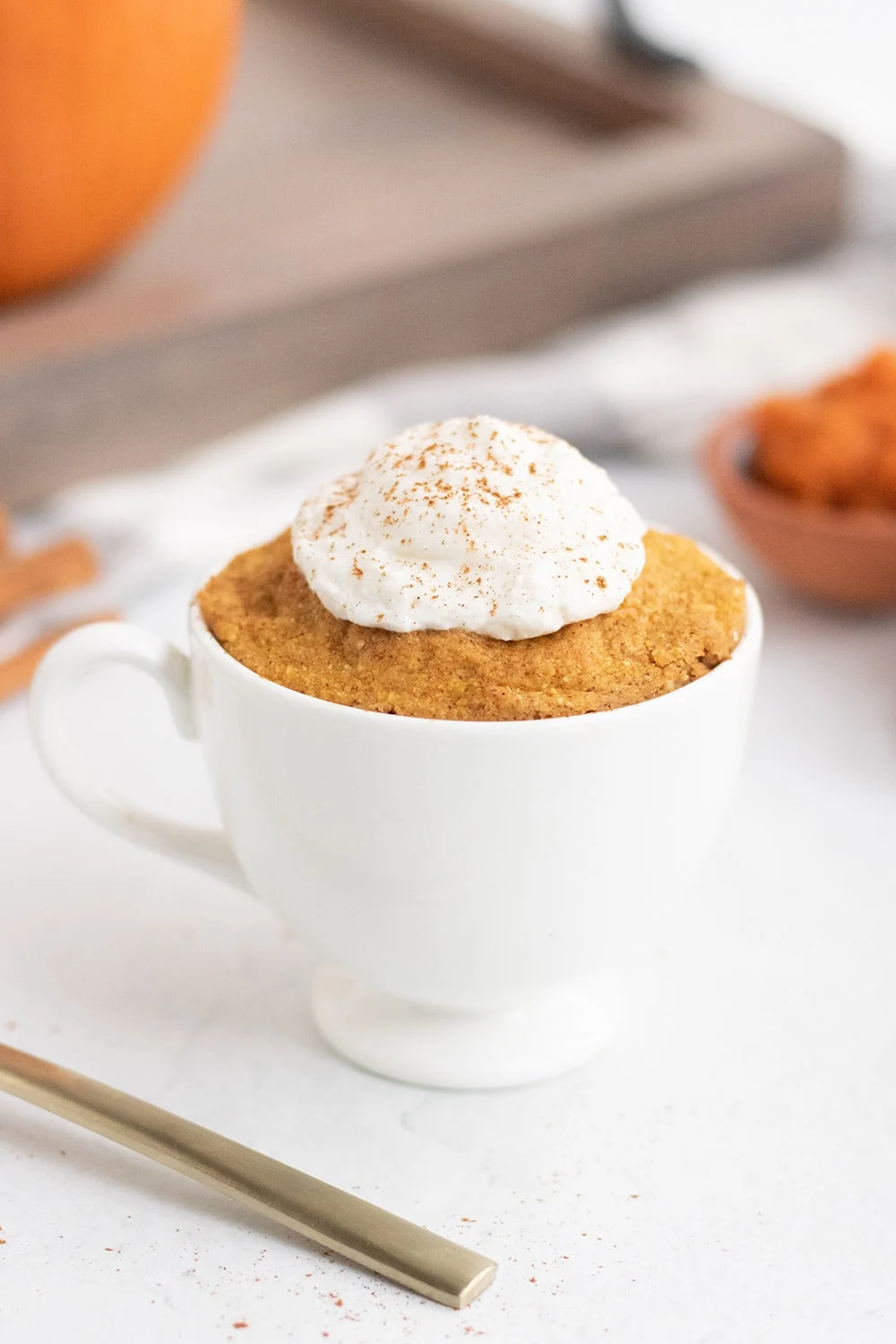 Pumpkin cake in a mug by a fork and a tray.