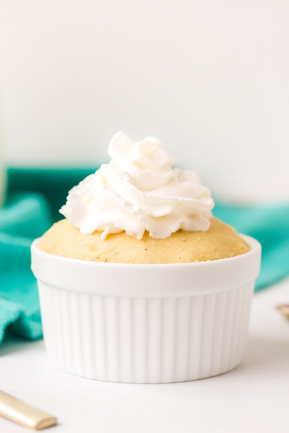 Keto vanilla mug cake topped with whipped cream by a green napkin.