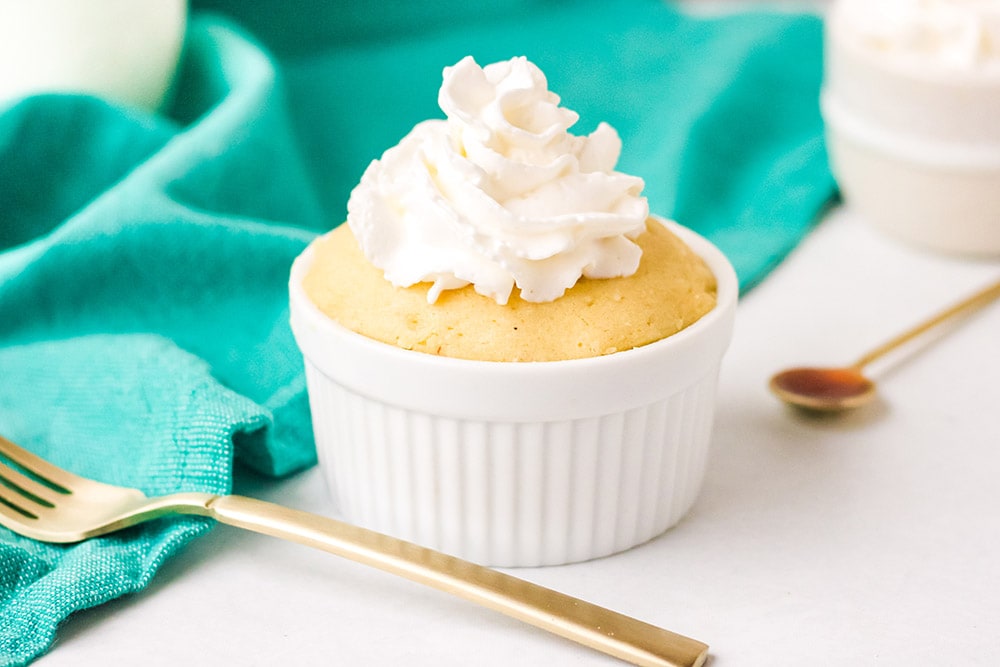 Vanilla mug cake with whipped cream next to a gold fork