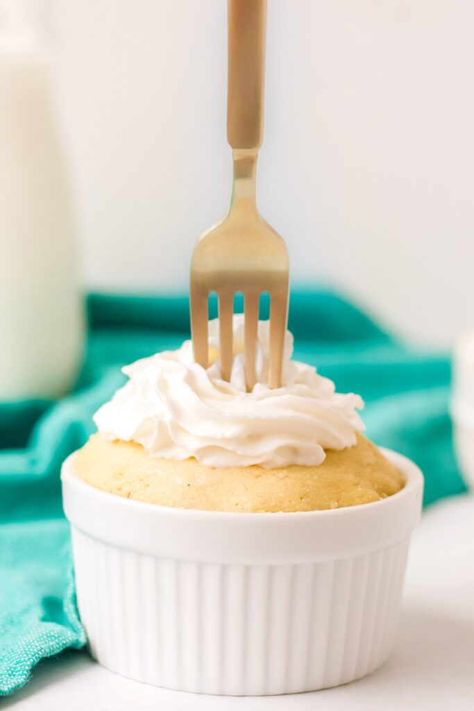 gold fork in a vanilla mug cake with whipped cream on a table with green napkin