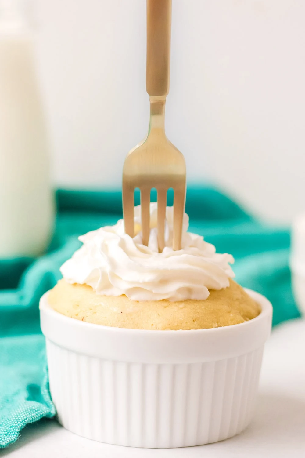 Gold fork in a vanilla mug cake with whipped cream on a table with green napkin.