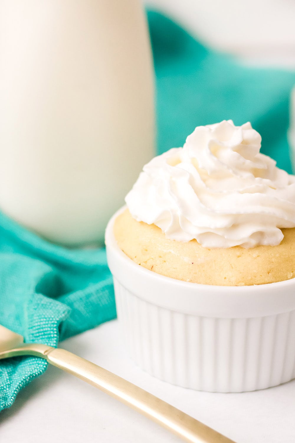 Low-carb vanilla mug cake next to a gold fork and glass of milk.