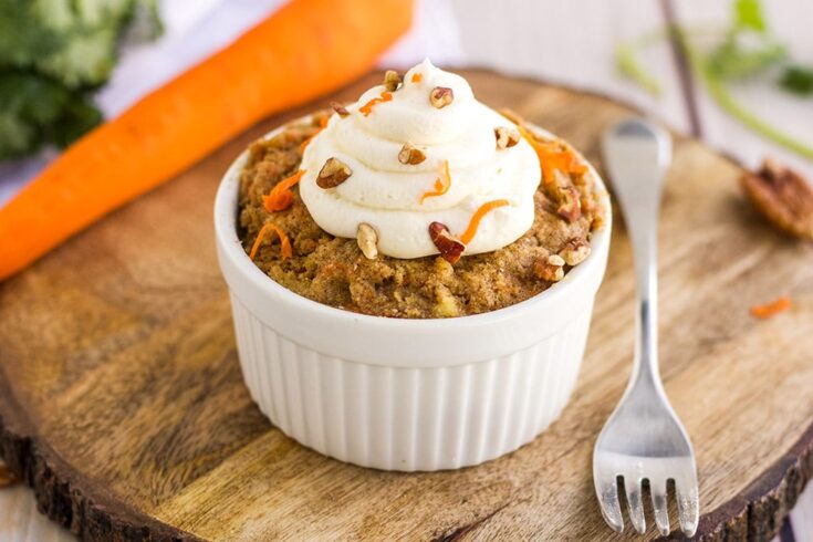 Carrot cake in a ramekin by a carrot and a fork on a board