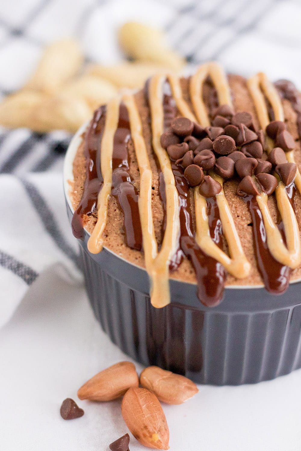 Chocolate peanut butter mug cake with drizzles and chips on a table. 
