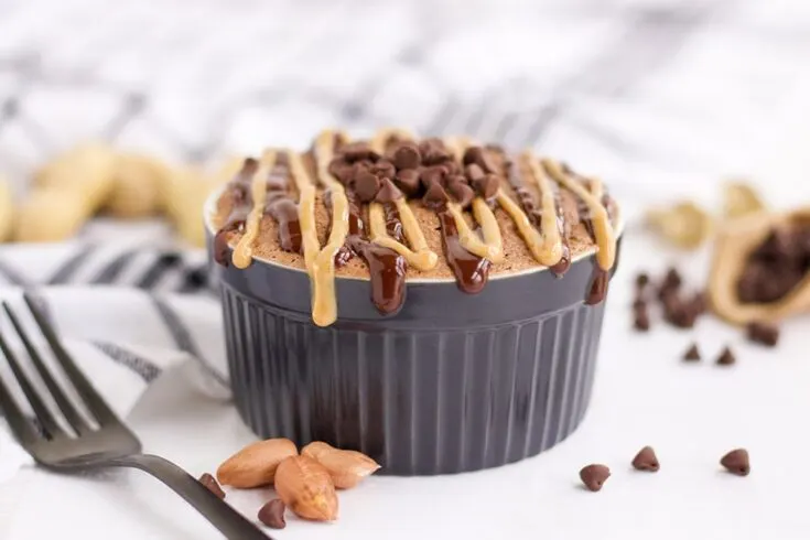 Chocolate peanut butter cake in a blue ramekin with peanuts and chocolate chips on the table.