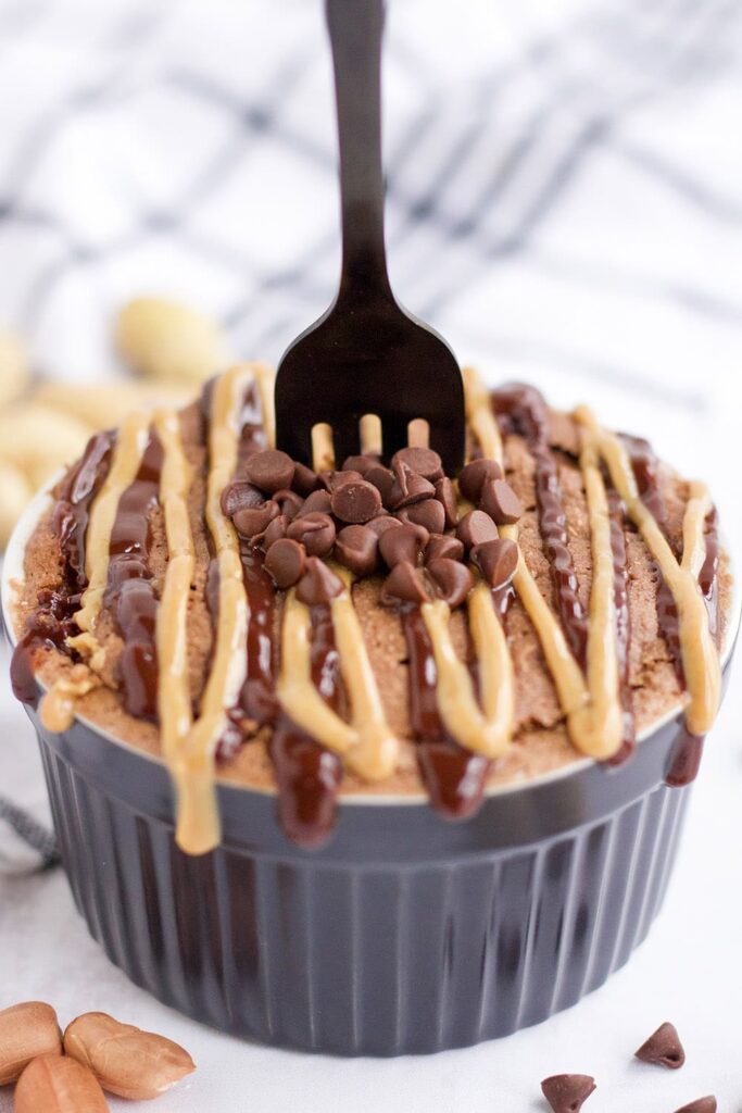 Fork stuck in a peanut butter chocolate mug cake with glaze and mini chips. 