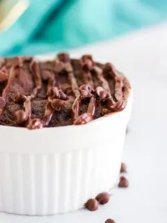 Brownie in a white ramekin by a teal napkin and chocolate chips.