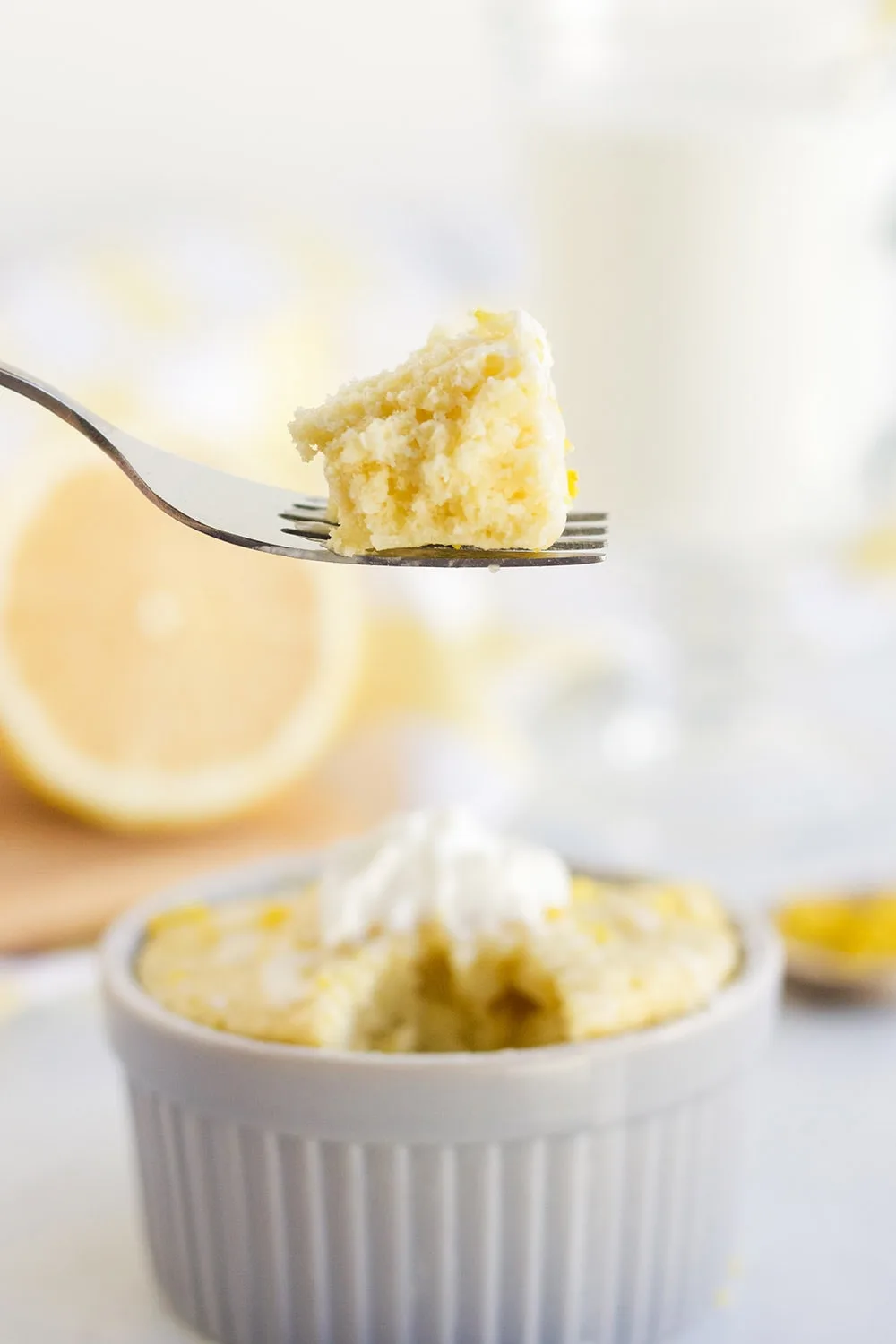 Lemon mug cake with cake on a fork and lemon in the background.