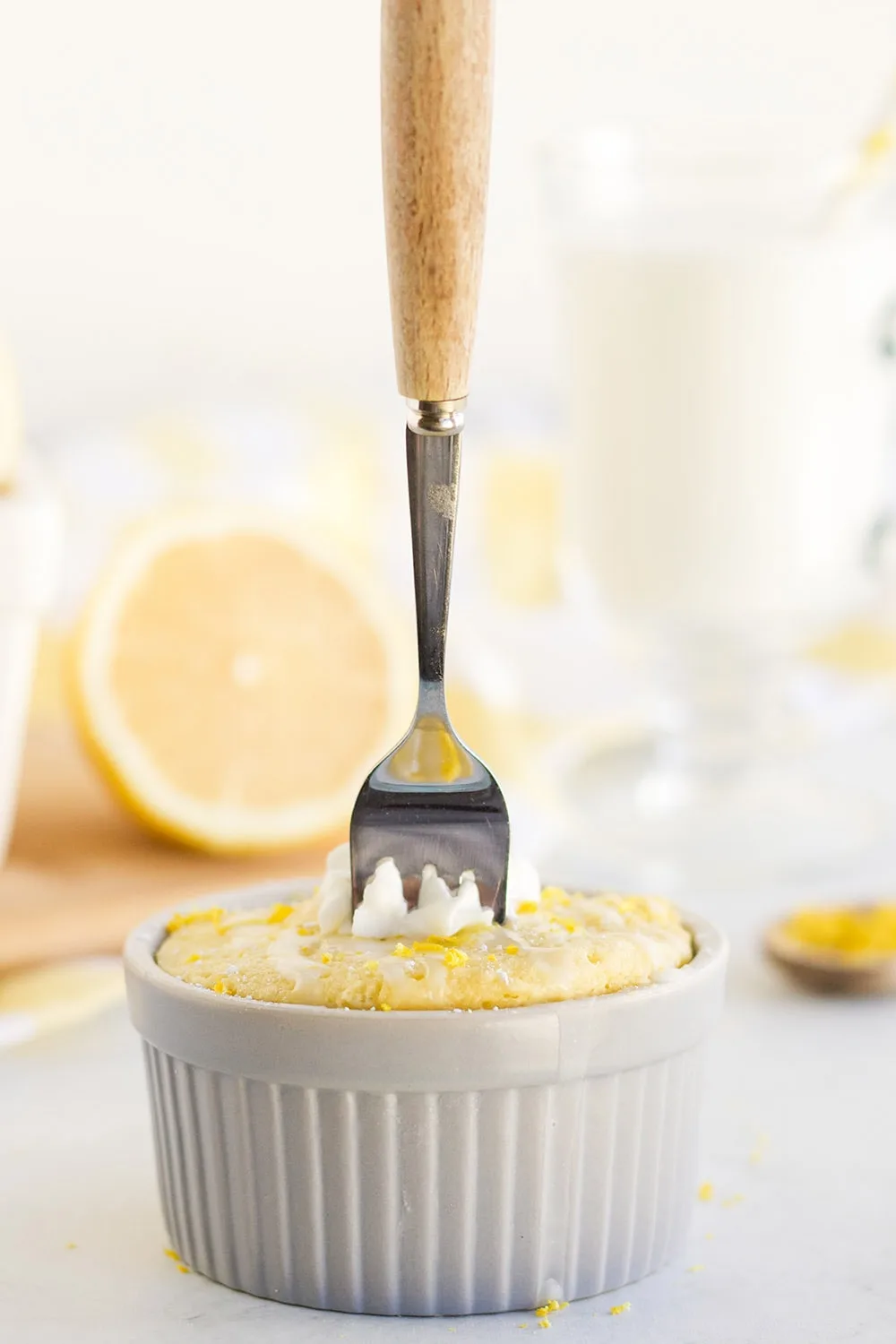 Fork stuck in a lemon cake in a grey ramekin.