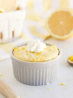 Lemon mug cake with whipped cream on a table with lemons.