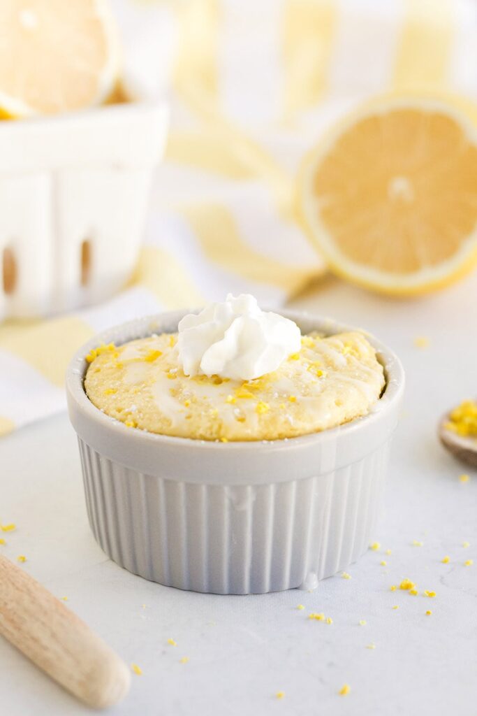 Lemon mug cake with whipped cream on a table with lemons. 