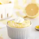 Low-carb lemon mug cake with whipped cream on a table with lemons.