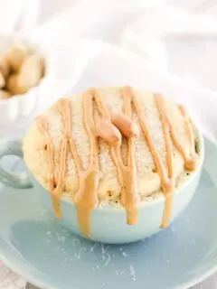 Peanut butter cake in a blue mug topped with drizzles and peanuts.