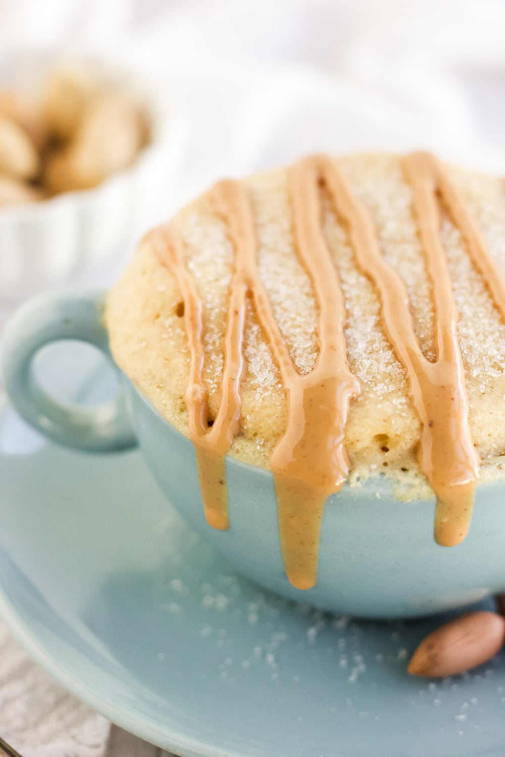 Peanut butter cake with drizzles in a blue mug by peanuts.