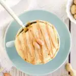 Overhead image of peanut butter cake in a mug topped with peanuts.