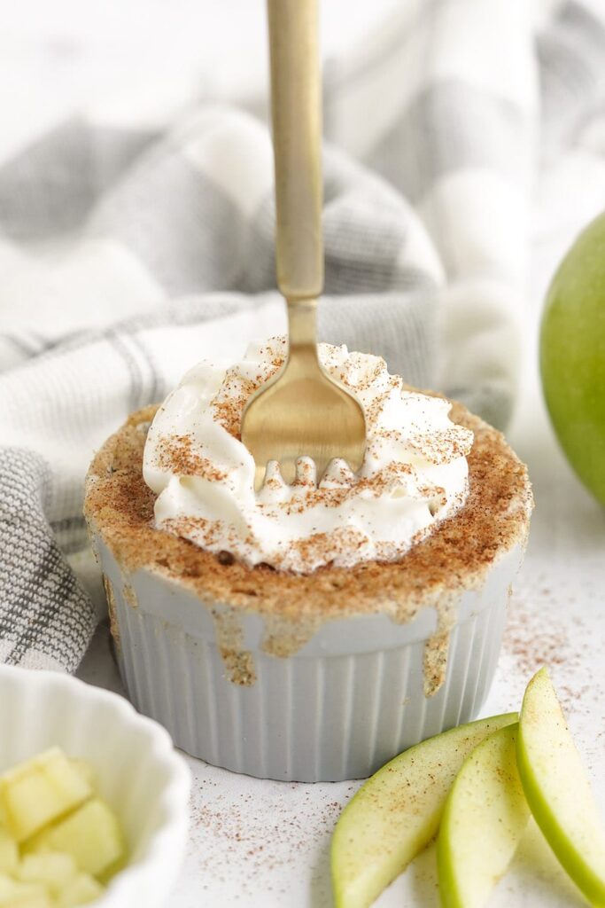 Fork in a cake in a small dish. There are green apples and slices on the table with a gray napkin.