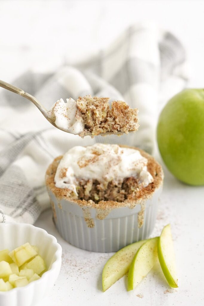 Fork full of apple cake in above the full cake with green apple slices.