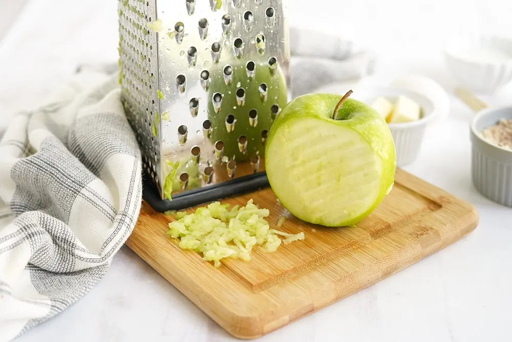Green apple with a shredder on a board.