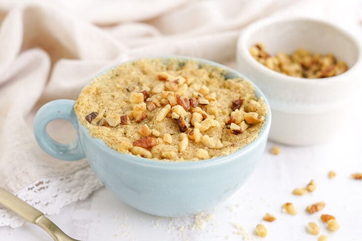 Banana cake in a blue mug with chopped walnuts.