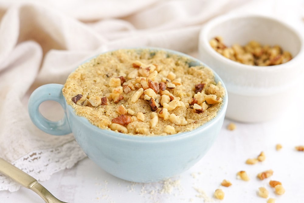 Banana cake in a blue mug with chopped walnuts.