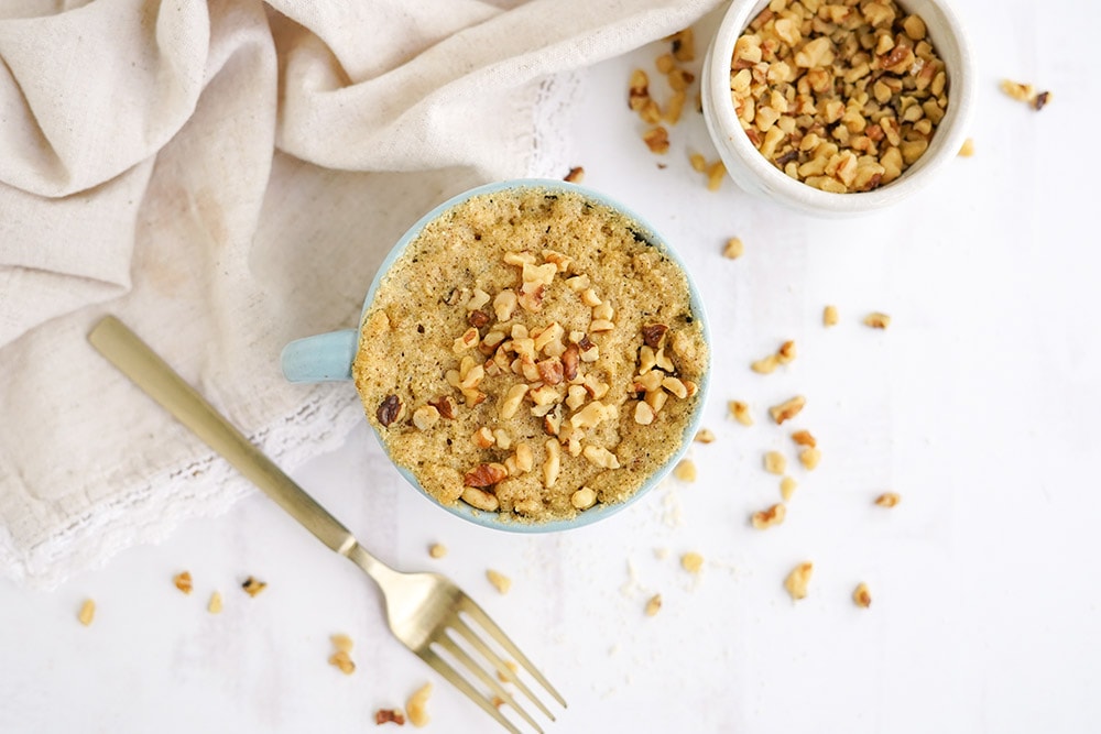 Banana cake topped with walnuts with chopped walnuts and a gold fork on the table.