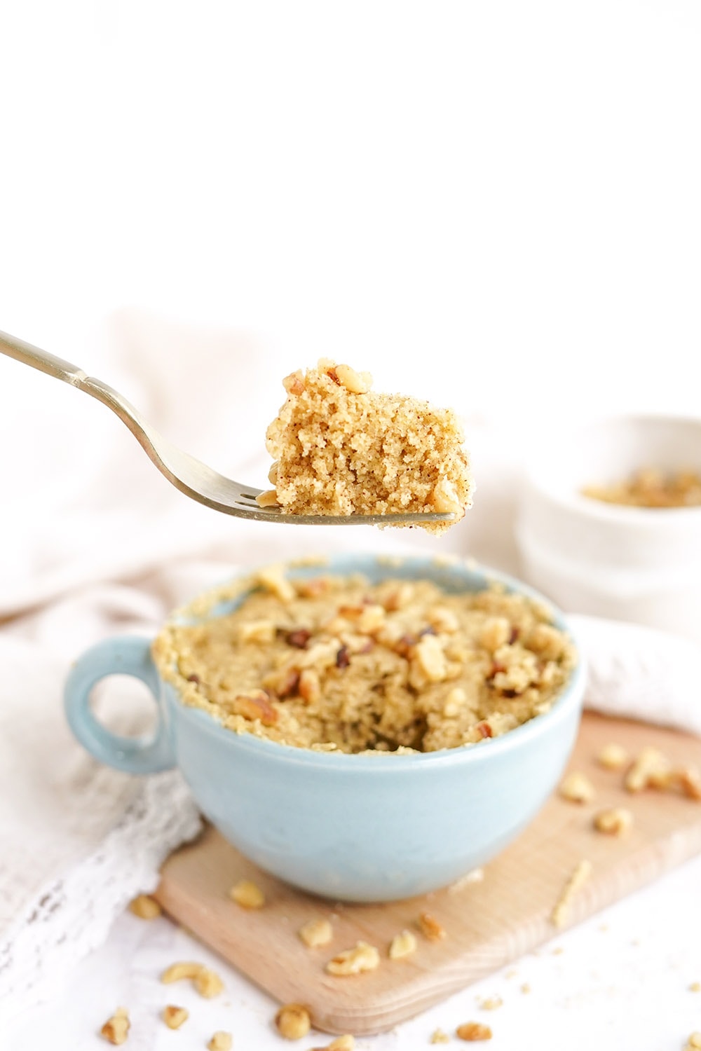 Fork full of banana cake raised about the rest of the cake in a light blue mug.