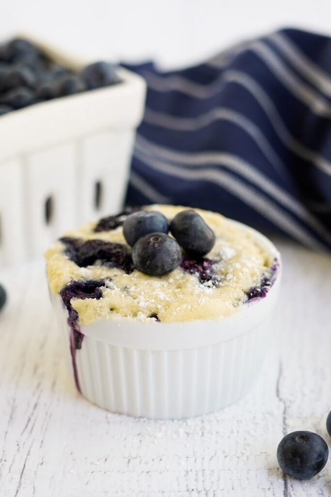 Fresh blueberries on top of a small cake in a white dish.