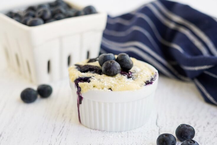 Small cake topped with blueberries on a white table with a navy napkin.