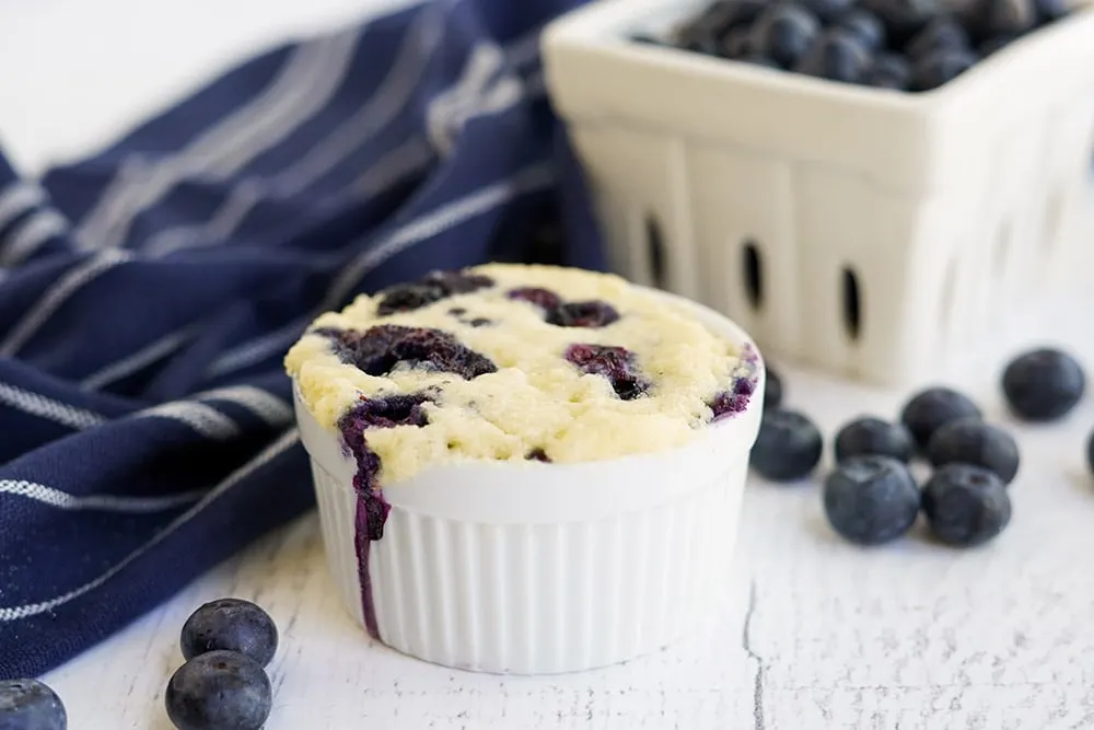 Tiny baked cake in a white dish with blueberries.
