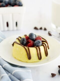 Small cheesecake on a white plate topped with berries and melted chocolate.