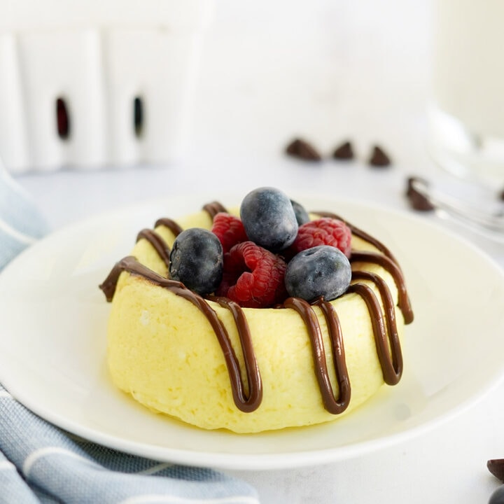 Small cheesecake on a white plate topped with berries and melted chocolate.