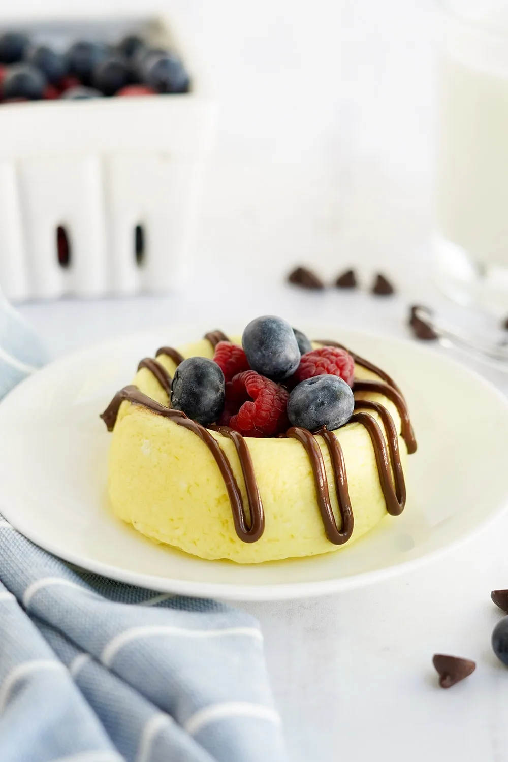 Small cheesecake on a white plate topped with berries and melted chocolate.