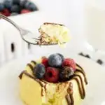 Raised fork with cake above a cheesecake with berries and chocolate.
