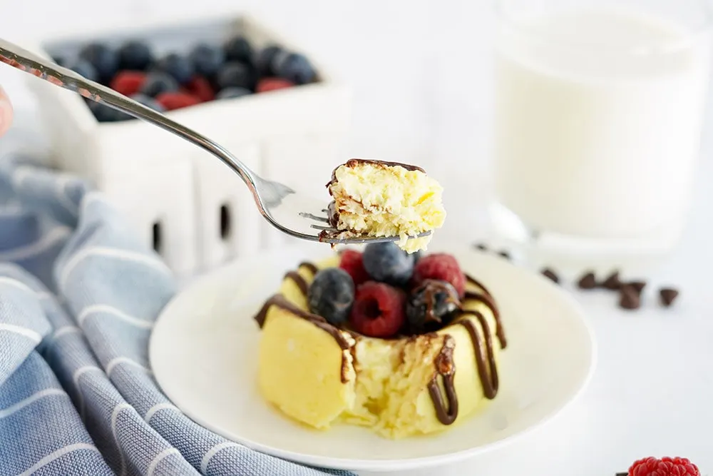 Fork full of cake above a cheesecake with berries and chocolate.