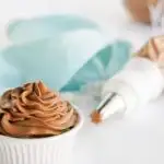 Piping bag with tip, blue napkin, and whipped chocolate topping on a white table.