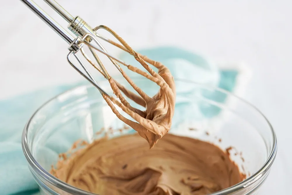 Raised mixer of chocolate whipped cream over a mixing bowl.