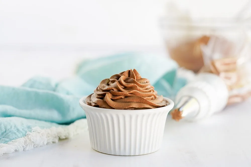 Chocolate whipped topping in a white dish with the piping bag and a light blue napkin on the table.