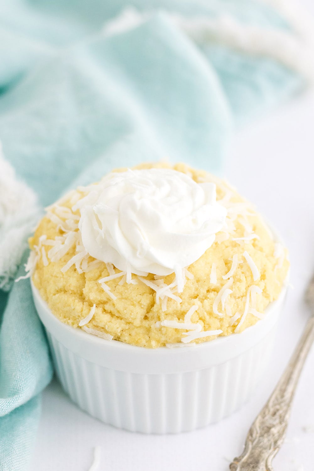 Coconut mug cake topped with shreds and whipped topping in a dish.